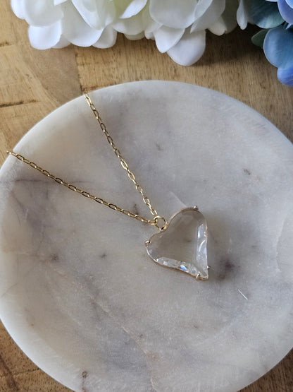 Primer plano detallado de un delicado collar con un dije de corazón de acrílico transparente tipo colgante.