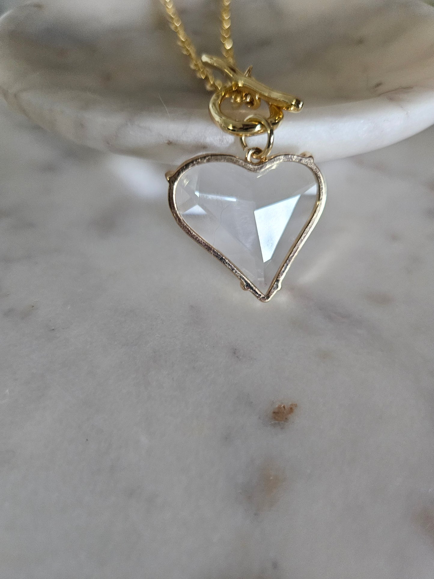 Primer plano detallado de un delicado collar con un dije de corazón de acrílico transparente, Colgando del cierre T-bar.