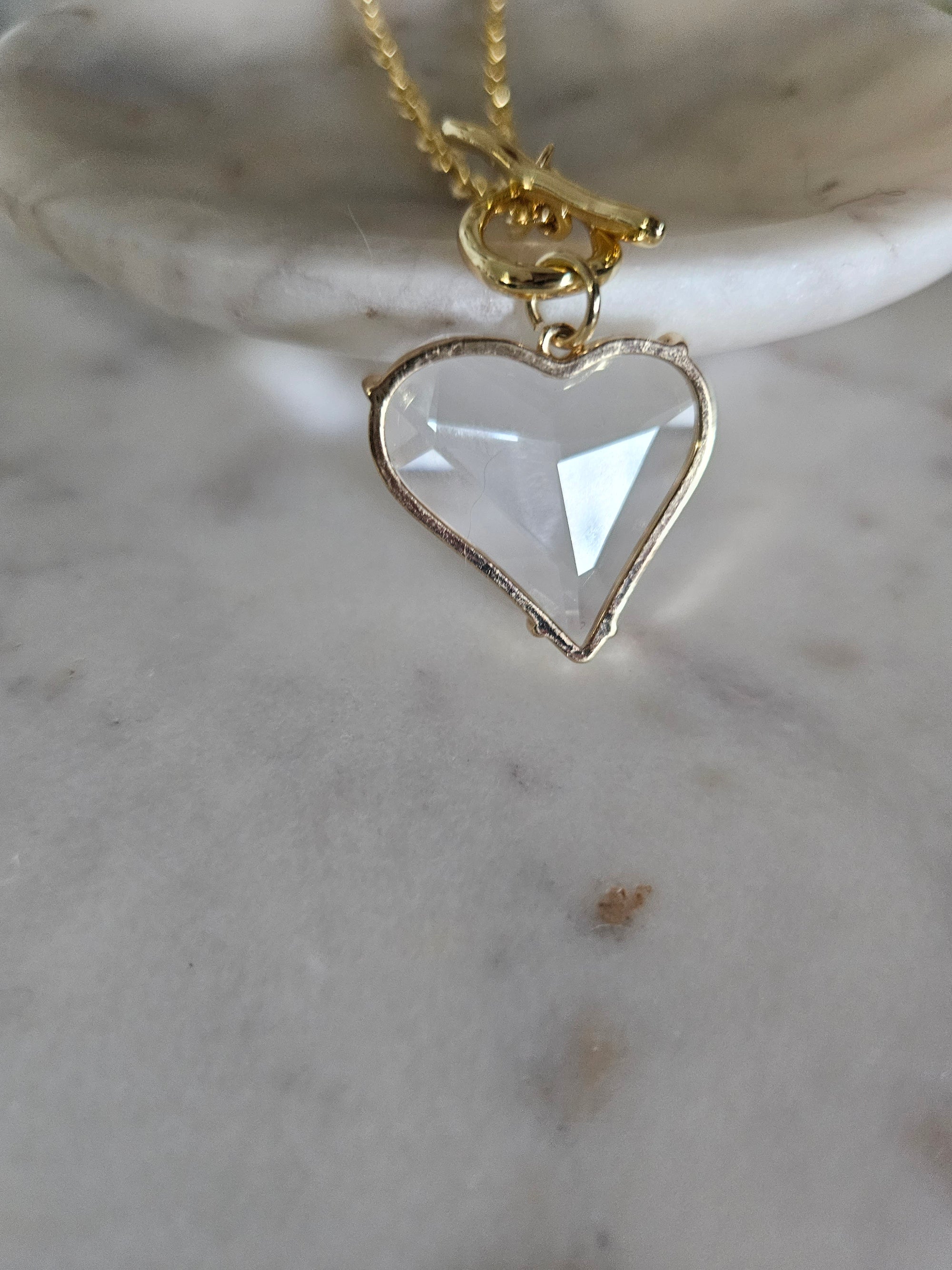 Primer plano detallado de un delicado collar con un dije de corazón de acrílico transparente, Colgando del cierre T-bar.