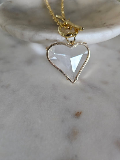 Primer plano detallado de un delicado collar con un dije de corazón de acrílico transparente, Colgando del cierre T-bar.