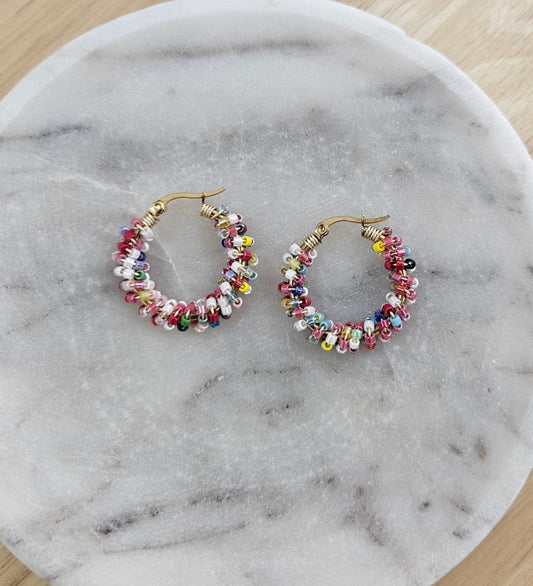 Argollas doradas con pequeñas cuentas Miyuki de múltiples colores tejidas alrededor.