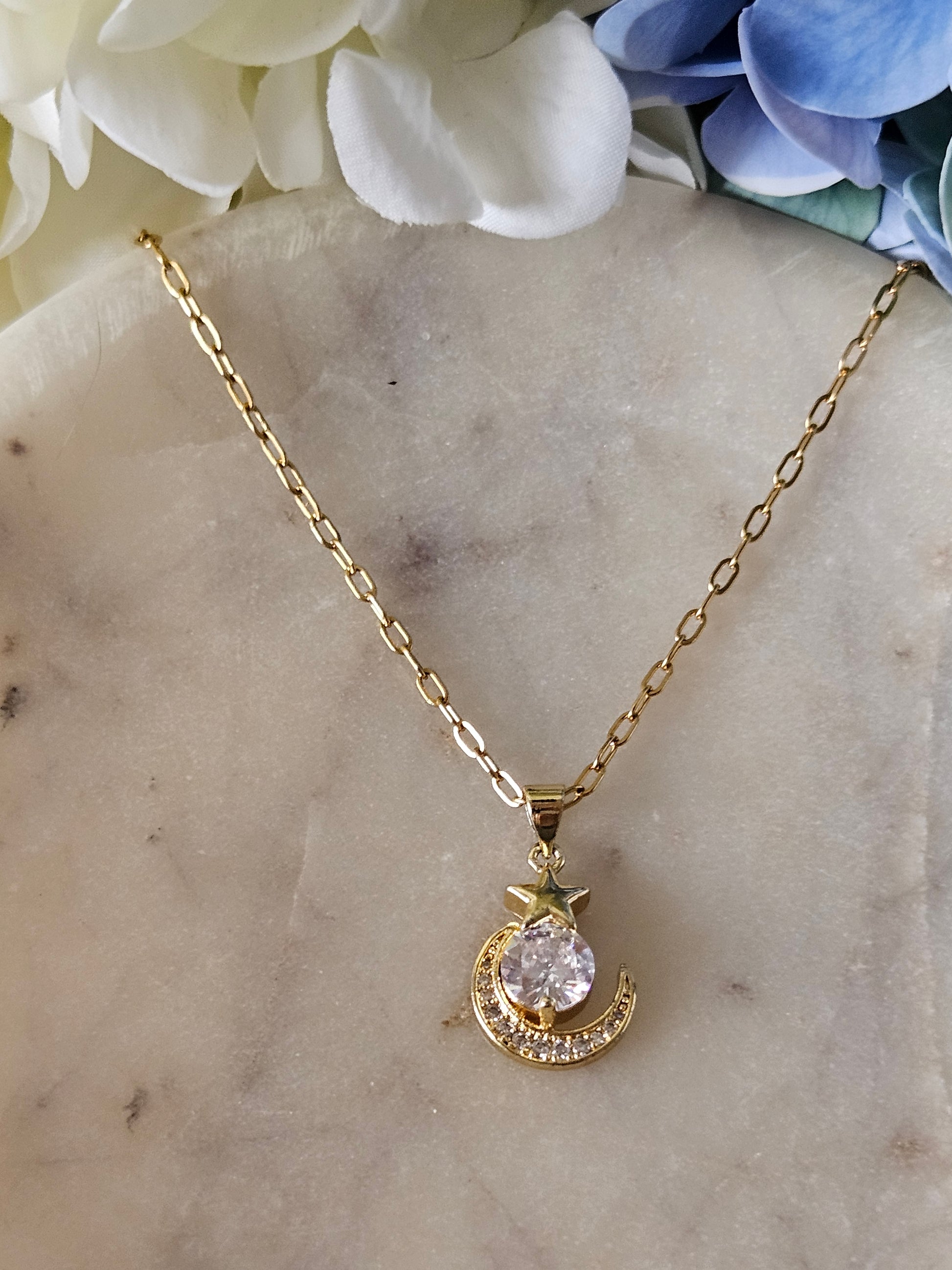 Collar dorado con una delicada cadena de eslabones. El dije representa una luna creciente dorada con pequeños cristales brillantes y una estrella también con cristales.