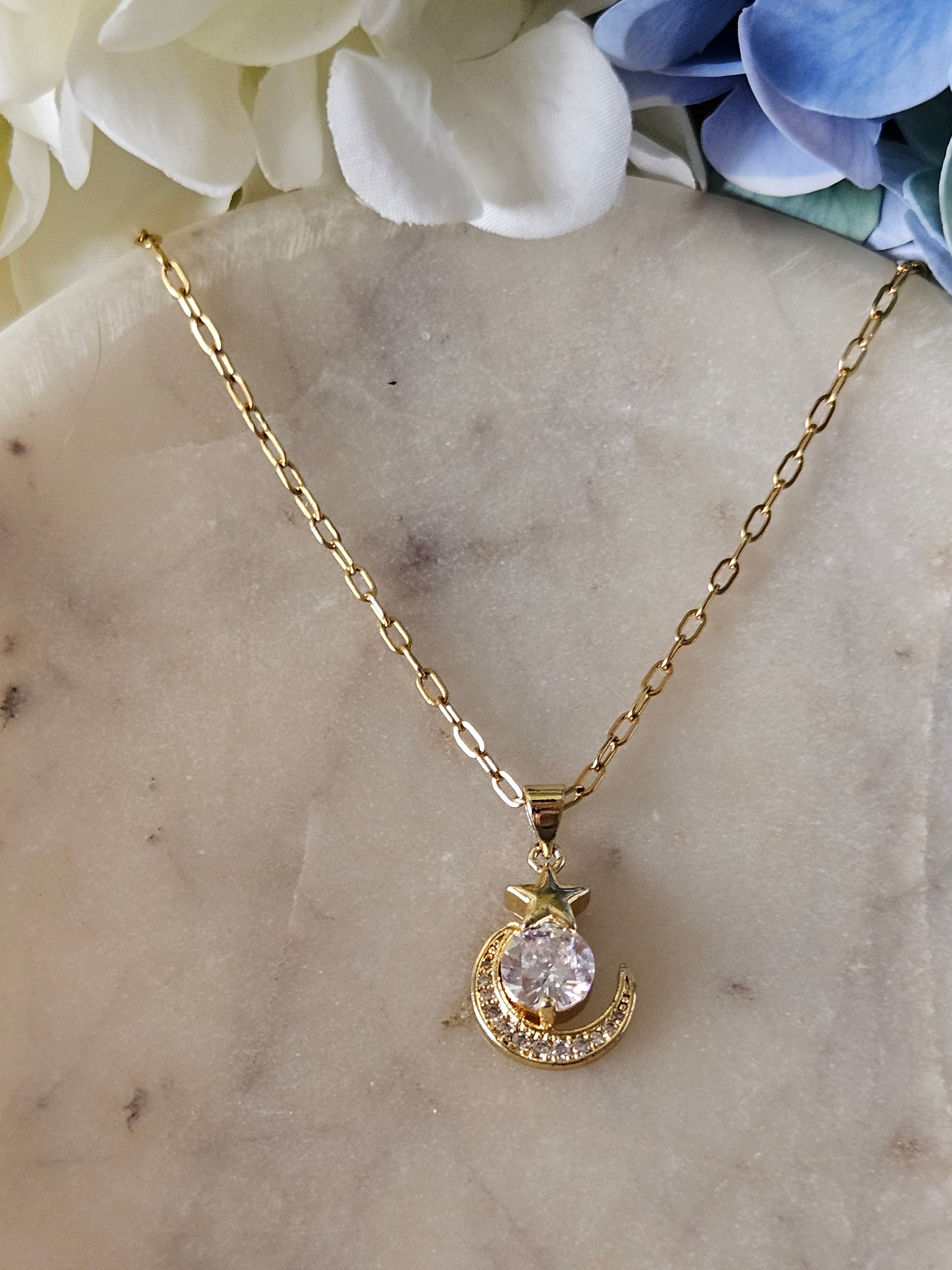 Collar dorado con una delicada cadena de eslabones. El dije representa una luna creciente dorada con pequeños cristales brillantes y una estrella también con cristales.