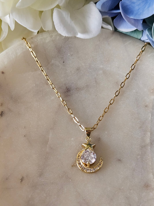 Collar dorado con una delicada cadena de eslabones. El dije representa una luna creciente dorada con pequeños cristales brillantes y una estrella también con cristales.