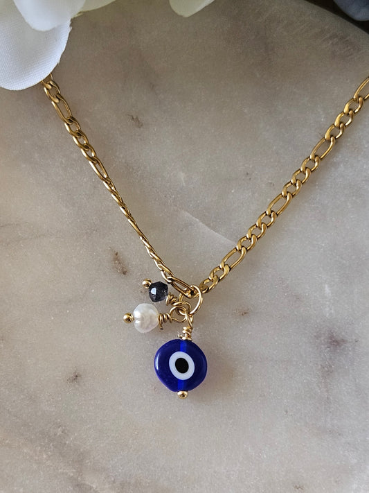 Collar Sabiduría Ancestral Mereki: detalle de la cadena Figaro dorada y los dijes de ojo turco azul, perla blanca y cristal.
