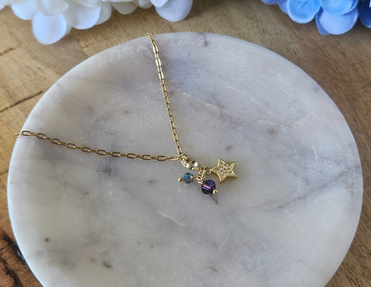 Collar dorado con una delicada cadena de eslabones. El dije es una estrella dorada con pequeños cristales azul ahumado y ciruela.