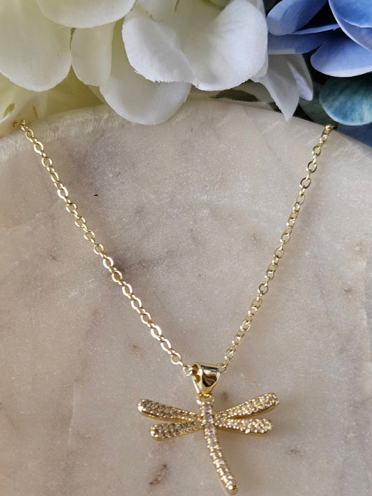 Collar dorado con una delicada cadena de eslabones. El dije es una libélula brillante, adornada con pequeños cristales blancos engastados en micro pavé.