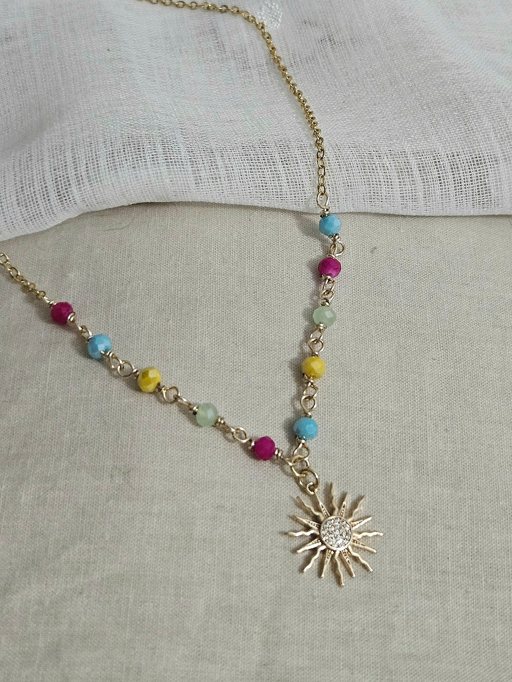 Collar dorado con una cadena que combina cuentas de colores engarzadas y eslabones. El dije es un sol dorado brillante con pequeñas piedras incrustadas en micro pavé.