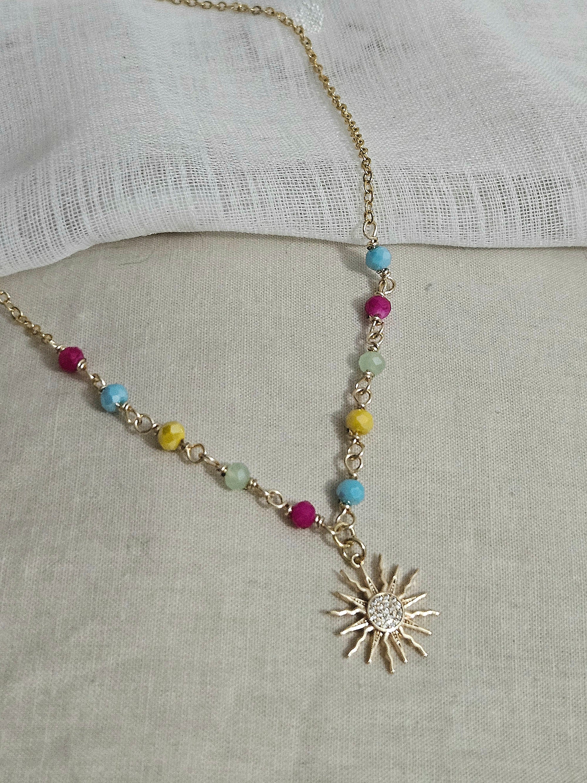 Collar dorado con una cadena que combina cuentas de colores engarzadas y eslabones. El dije es un sol dorado brillante con pequeñas piedras incrustadas en micro pavé.