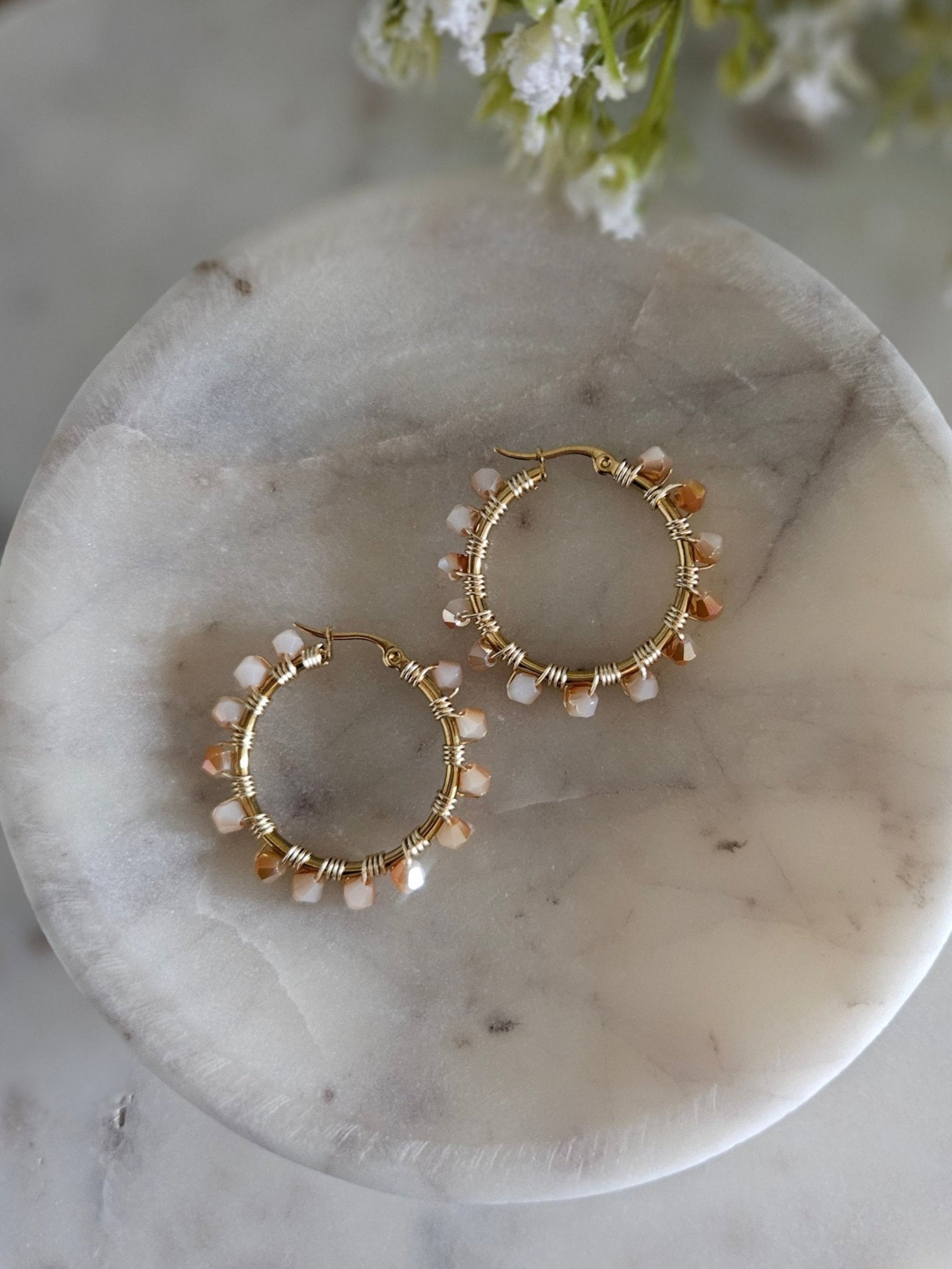 Detalle cercano de unos aros dorados con cristales crema y blancos arremolinados, capturando su brillo suave.